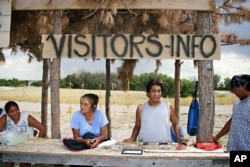 In a Friday, July 20, 2012, photo, from the left; Tricia Bear Eagle, Helen Red Feather, Rudell Bear Shirt and Edward Jealous Of Him, all of Wounded Knee, S.D., wait for tourists near the site of the Wounded Knee Massacre on the Pine Ridge Indian Reservati