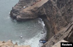 A helicopter helps rescue workers at the scene after a bus crashed with a truck and careened off a cliff along a sharply curving highway north of Lima, Peru, Jan. 2, 2018.