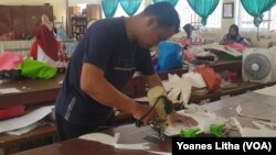 Seorang guru yang sedang memotong bahan untuk pembuatan baju alat perlindungan diri (APD) yang diproduksi di SMK Negeri 5 Palu, 31 Maret 2020. (Foto: VOA/Yoanes Litha)