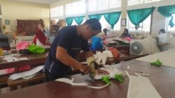 Seorang guru yang sedang memotong bahan untuk pembuatan baju alat perlindungan diri (APD) yang diproduksi di SMK Negeri 5 Palu, 31 Maret 2020. (Foto: VOA/Yoanes Litha)