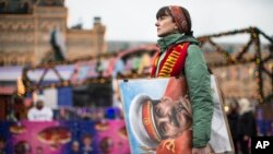 FILE - An artist holds a portrait of former Soviet leader Josef Stalin as Communist Party supporters marking the anniversary of Stalin's birth outside the GUM department store, decorated with New Year and Christmas illumination, in Moscow's Red Square, Russia, Dec. 21, 2017. Russia's Culture Ministry Jan. 23, 2018, banned a satirical film about Stalin's death, two days before its scheduled release.