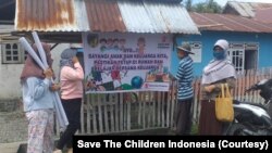 Warga di desa Dampal, Kecamatan Sirenja, Donggala yang sedang membaca baliho berisi imbauan untuk mengajak anak tetap belajar bersama keluarga di rumah. (Foto: Save The Children Indonesia)