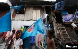 Boys hold flags of the ruling Cambodian People's Party (CPP) outside a house at a slum area in Phnom Penh July 23, 2013.
