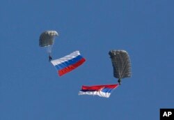 FILE - Serbian soldiers parachute from a Mi-8 transport helicopter with a Russian, left, and Serbian flags during joint Russian-Serbian military exercices at Nikinci training ground, 60 kilometers west of Belgrade, Serbia, Nov. 14, 2014.