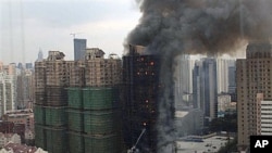 Firefighters spray water on an apartment building on fire in the downtown area of Shanghai, east China, on 15 Nov 2010