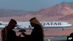FILE - Journalists chat as video of a plane carrying Qatar's emir, Sheikh Tamim bin Hamad al-Thani, is shown on a screen while landing at al-Ula airport, where the 41st Gulf Cooperation Council meeting takes place, in Saudi Arabia, Jan. 5, 2021.
