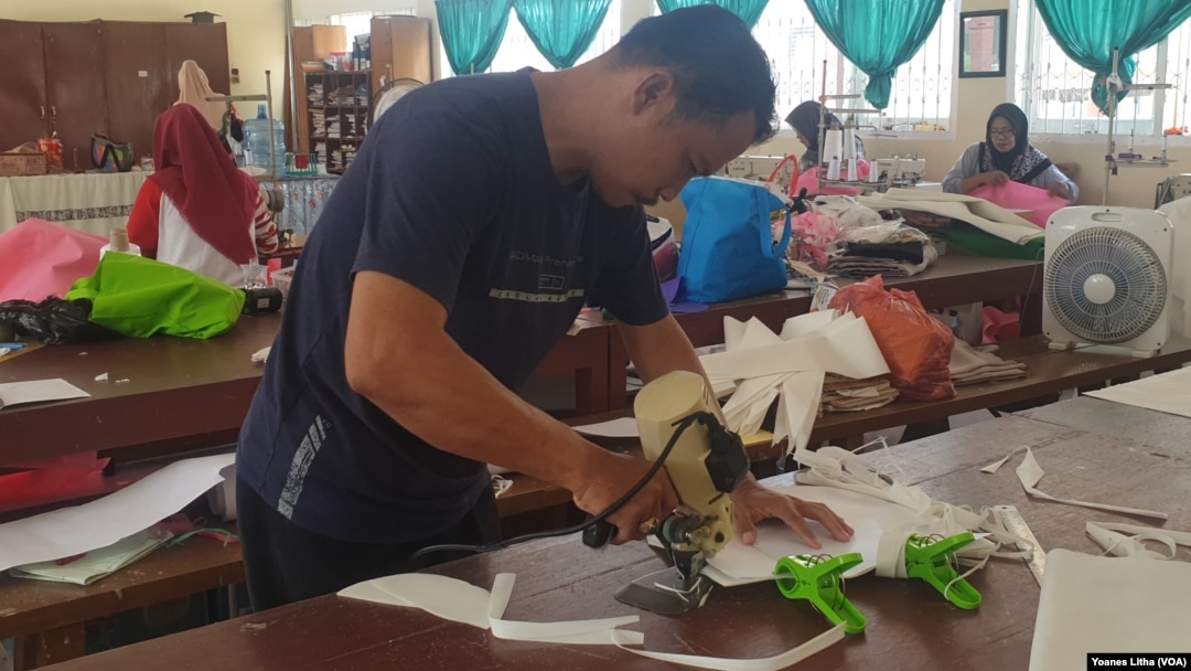 Seorang guru yang sedang memotong bahan untuk pembuatan baju alat perlindungan diri (APD) yang diproduksi di SMK Negeri 5 Palu, 31 Maret 2020. (Foto: VOA/Yoanes Litha)