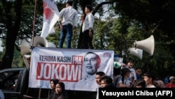 Massa pendukung pemerintah membentangkan poster bertuliskan ucapan terima kasih kepada Presiden Joko Widodo, dua hari menjelang pelantikan Presiden terpilih Prabowo Subianto, Jumat, 18 Oktober 2024. (Foto: Yasuyoshi Chiba/AFP)