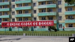 FILE - A woman walks outside an apartment building where an anti-U.S. propaganda banner is put up in Pyongyang, North Korea, June 21, 2018.