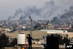 Seorang pria mengambil gambar dari atap saat asap mengepul di atas Khan Yunis di jalur Gaza selatan selama pengeboman Israel pada 17 Desember 2023. (Foto: AFP)