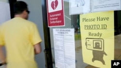 FILE - A voter walks past a "Please Have Photo ID Ready" sign as he enters an early-voting polling place in downtown Little Rock, Arkansas, May 5, 2014.