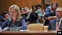 FILE - Women carrying children in their arms stand up to protest Homeland Security Secretary Kirstjen Nielsen, left, during Nielsen's opening remarks before Senate Appropriations subcommittee hearing on Capitol Hill in Washington, May 8, 2018. 