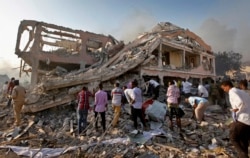 FILE - Somalis gather and search for survivors by destroyed buildings at the scene of a blast in the capital Mogadishu, Somalia, Oct. 14, 2017.