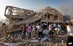 Somalis gather and search for survivors by destroyed buildings at the scene of a blast in the capital Mogadishu, Somalia, Oct. 14, 2017.