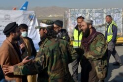 Anggota Taliban dan staf bandara berdiri di samping kiriman vaksin COVID-19 sumbangan dari pemerintah China di bandara Kabul di Kabul, 8 Desember 2021. (AHMAD SAHEL ARMAN / AFP)