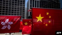 Pedestrians walk near Hong Kong and Chinese flags in Hong Kong on June 29, 2023, ahead of the 26th anniversary of the city’s handover from Britain to China on July 1. (Photo by ISAAC LAWRENCE / AFP)