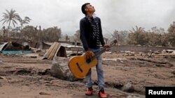 Brian Rivera, who lost 13 members of his family during the eruption of the Fuego volcano, holds his sister's guitar near debris of his home at San Miguel Los Lotes, Escuintla, Guatemala, June 7, 2018. 
