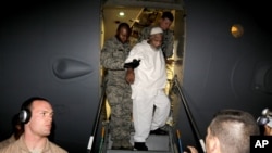 Ibrahim Idris, is escorted off a U.S. military plane by after his release from Guantanamo Bay, upon his arrival at the airport in Khartoum, Sudan, Thursday, Dec. 19, 2013 (AP Photo/Abd Raouf)