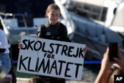 Climate activist Greta Thunberg holds a sign reading 'School strike for the climate' after arriving in Lisbon, aboard the sailboat La Vagabonde, Dec 3, 2019.