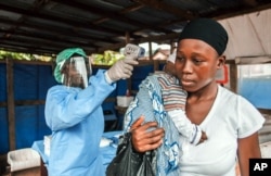 FILE - A woman has her temperature taken as part of Ebola prevention, prior to entering the Macauley government hospital in Freetown, Sierra Leone, Jan. 21, 2016.