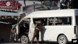 An Afghan security forces member inspects a bus carrying local TV station employees that hit a roadside bomb in Kabul, Afghanistan, Saturday, May 30, 2020. 