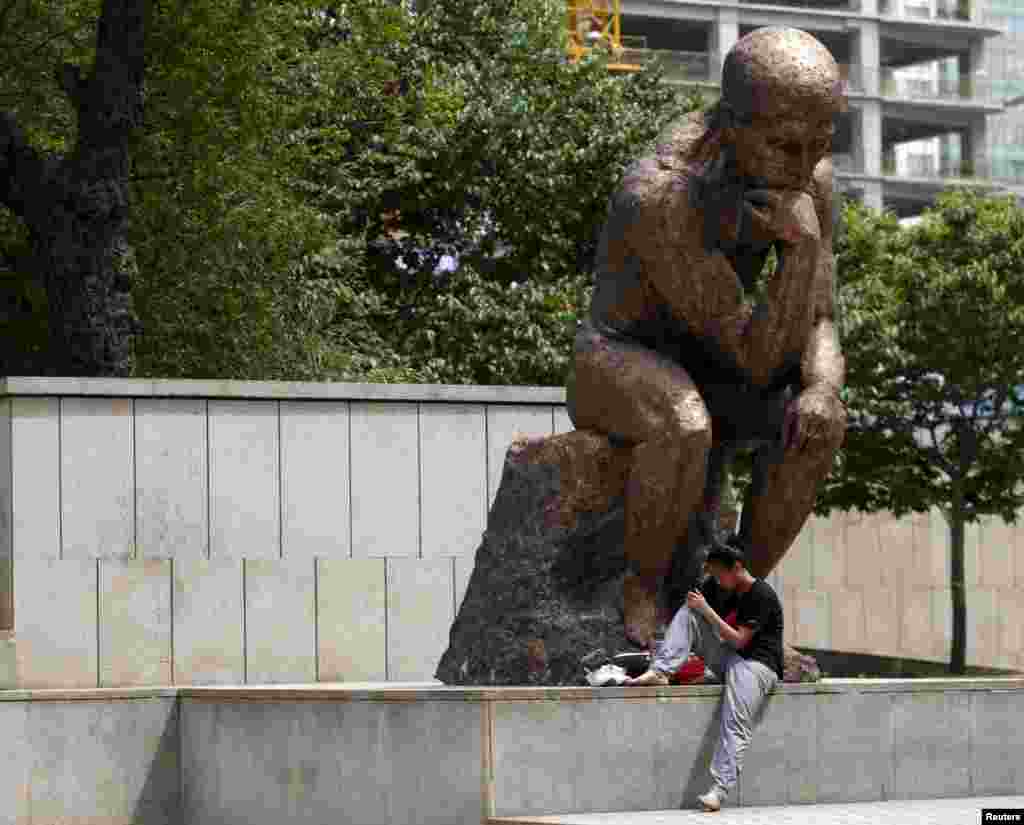 A woman sits underneath a sculpture at a financial district in Beijing, China, May 5, 2015.