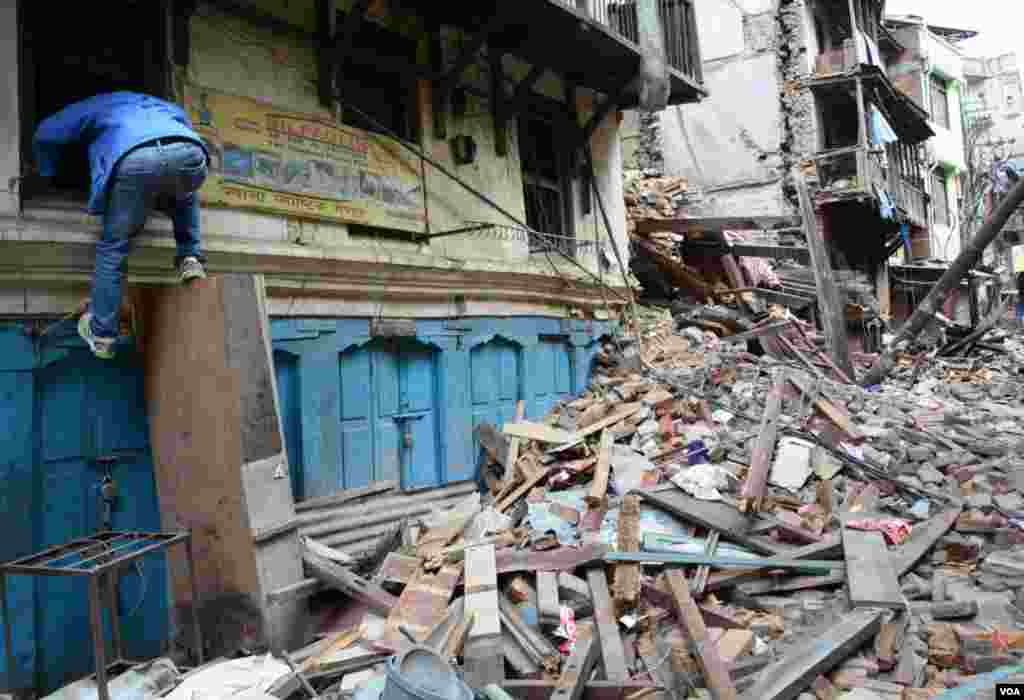 A man exits his home through the window after removing some of his property, Tyouda, Asan, Kathmandu, April 27, 2015. (Bikas Rauniar/VOA)