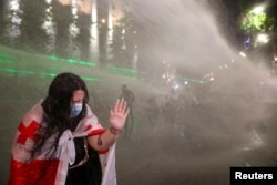 FILE - A woman reacts as law enforcement officers use a water cannon to disperse the crowd near the parliament building, during a rally to protest against a bill on "foreign agents" in Tbilisi, Georgia, May 1, 2024.