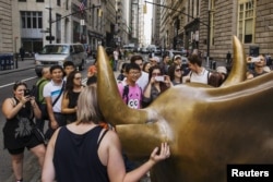 FILE - Tourists pose for photographs with a landmark statue of a bull in New York, Aug. 24, 2015.