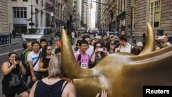 Para turis berpose di depan patung banteng di kawasan Wall Street, New York (foto: dok).