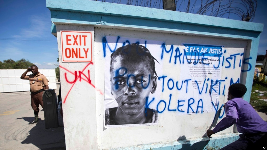 A demonstrator spray paints the message in Creole "We demand justice for all cholera victims" outside United Nations headquarters to protest the U.N. peacekeeping mission in Port-au-Prince, Haiti, Oct. 15, 2015. 