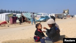 Seorang anak perempuan Palestina tampak menyuapi adiknya makanan di dekat tenda pengungsi di Rafah, tempat mereka kini tinggal, pada 25 Februari 2024. (Foto: Reuters/Saleh Salem)