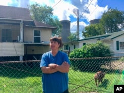 In this Aug. 23, 2018 photo, Andrea Maxey of Poca, West Virginia, speaks outside her home with the American Electric Power’s John Amos coal-fired power plant is in the background across the Kanawha River in Winfield.