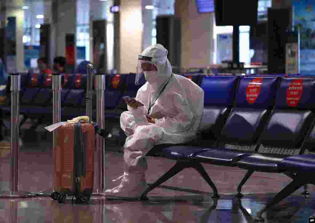 A passenger in a full protective suit uses a phone while waiting to board a flight at Tan Son Nhat airport in Ho Chi Minh city, Vietnam.