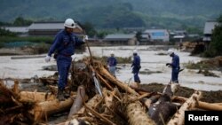 Pihak kepolisian Jepang berjalan di atas puing-puing kayu yang tersapu hujan lebat saat mereka melakukan operasi penyelamatan dan pencarian di Asakura, Prefektur Fukuoka, Jepang, 8 Juli 2017.