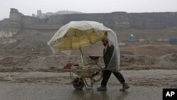 FILE - A vendor pushes his makeshift cart under a plastic cover in the rain, on the outskirts of Kabul, Afghanistan, Jan. 30, 2017. 