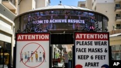 FILE - Signs with social distancing guidelines and face mask requirements are posted following a surge in COVID-19 cases led by the highly transmissible delta variant, at an outdoor mall in Los Angeles, June 11, 2021. 