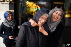 Syrian refugee Nada Alshebli, right, jokingly places a 'hijab' veil on Uruguayan Sonia de Leon as her sister Fatima walks behind them on a stroll through Juan Lacaze, Uruguay.