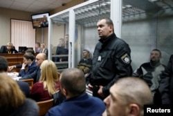 Former riot police officers, suspected of killing protesters during the Maidan revolt of 2014, sit inside a glass-walled room during a court hearing in Kyiv, Ukraine, Monday, Nov. 28, 2016.
