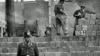 1961年10月7日,一名西柏林卫兵站在分隔东西柏林的混凝土墙前，同时，东德工人在为这道墙添砖加高。（资料照片）