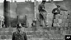 A West Berlin guard stands in front of the concrete wall dividing East and West Berlin at Bernauer Strasse, as East Berlin workmen add blocks to the wall to increase the height of the barrier, October 7, 1961 (file photo)