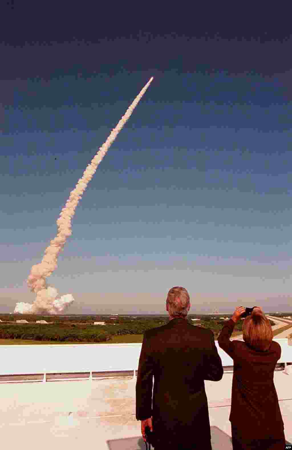 From the roof of the Launch Control Center, then U.S. President Bill Clinton and Hillary Clinton track the plume and successful launch of space shuttle Discovery on mission STS-95, October 29, 1998. (NASA) 