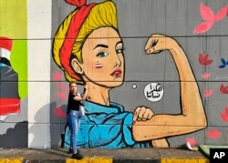In this Monday, Nov. 18, 2019 photo, a woman poses for a photo in front of graffiti at the Saadoun tunnel, in Baghdad, Iraq. The tunnel that passes under Baghdad's landmark Tahrir Square has become an ad hoc museum for Iraq's revolution: Young artists dra
