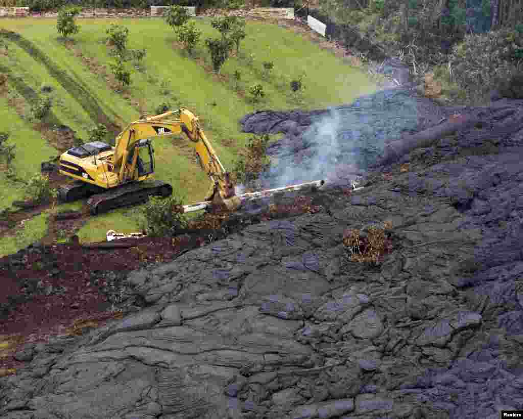 Seorang pekerja konstruksi mencoba menghambat aliran lahar dari Gunung Kilauea di Pahoa, Hawaii, dengan alat berat (29/10). 