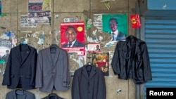 Election posters share wall space with a street trader's jackets, ahead of a presidential election, in Lusaka, Jan. 14, 2015.