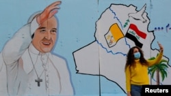 IRAQ - A woman takes selfies with a mural of Pope Francis on the wall of a church upon his upcoming visit to Iraq, in Baghdad, Iraq, February 22, 2021.