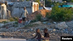 A Haitian man (L) carries a bucket filled with waste to be discarded, in a slum area in Port-au-Prince, Haiti, Dec. 17, 2012.