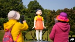 Visitantes toman fotos cerca de un modelo de la muñeca 'Younghee', de la serie de Netflix "Squid Game", que se exhibe en el parque olímpico de Seúl, el 26 de octubre de 2021. 