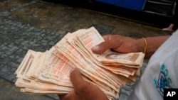 En esta imagen de archivo, tomada el 5 de agosto de 2021, un hombre cuenta billetes por el equivalente a un dólar en una parada de autobús en Caracas, Venezuela. Foto AP.