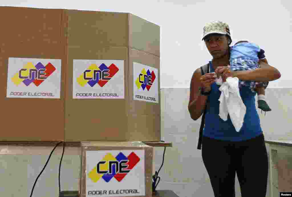 Una mujer lleva cargado a su hijo mientras emite su voto. 